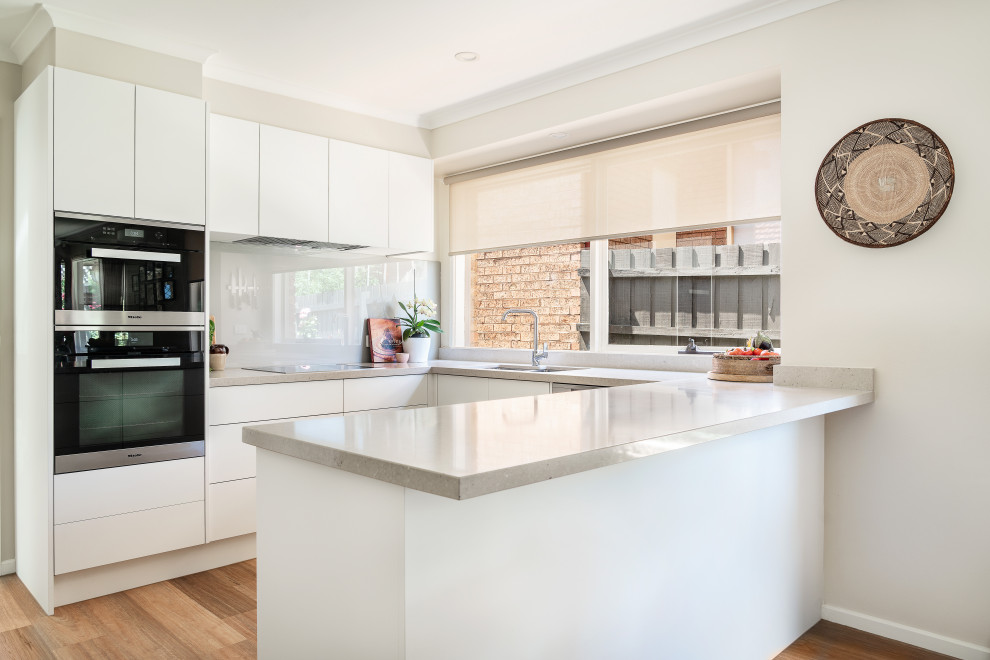 Design ideas for a medium sized contemporary u-shaped kitchen pantry in Melbourne with a double-bowl sink, white cabinets, engineered stone countertops, beige splashback, glass tiled splashback, black appliances, vinyl flooring, grey floors and beige worktops.