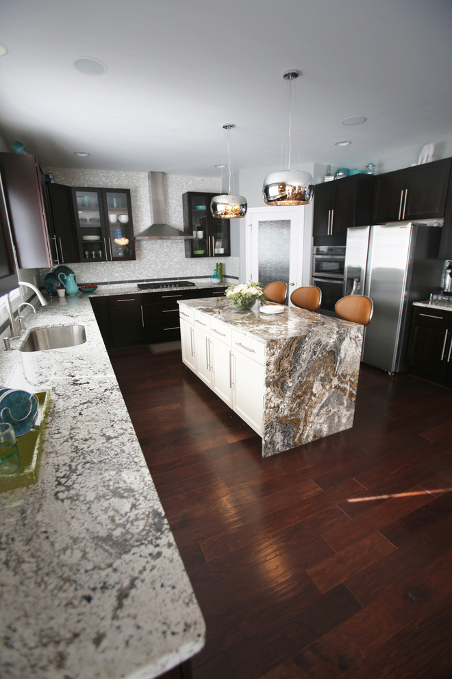 Photo of a large l-shaped eat-in kitchen in Detroit with a single-bowl sink, shaker cabinets, dark wood cabinets, granite benchtops, white splashback, porcelain splashback, stainless steel appliances, dark hardwood floors, with island and brown floor.