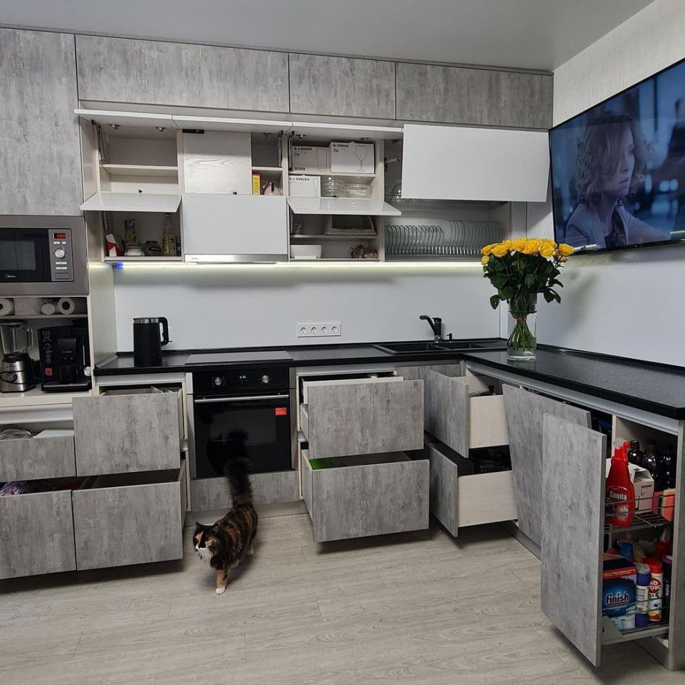 Large scandinavian l-shaped eat-in kitchen in Novosibirsk with a drop-in sink, flat-panel cabinets, grey cabinets, solid surface benchtops, white splashback, limestone splashback, black appliances, laminate floors, no island, yellow floor and black benchtop.