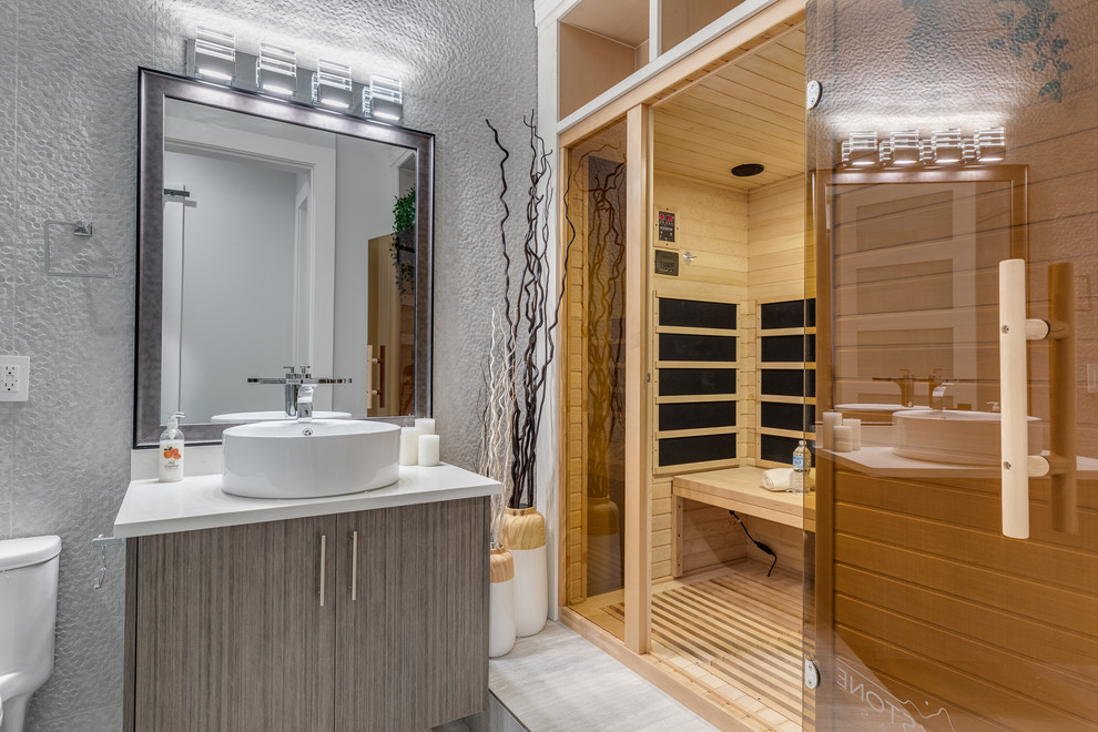 Inspiration for a large contemporary bathroom in Vancouver with flat-panel cabinets, grey cabinets, grey walls, with a sauna, a vessel sink, grey floor, a freestanding tub, an alcove shower, white tile, marble, marble floors, solid surface benchtops and a hinged shower door.