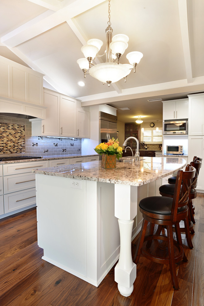 Photo of a large traditional l-shaped open plan kitchen in Dallas with shaker cabinets, white cabinets, granite benchtops, grey splashback, subway tile splashback, stainless steel appliances, medium hardwood floors, with island and an undermount sink.