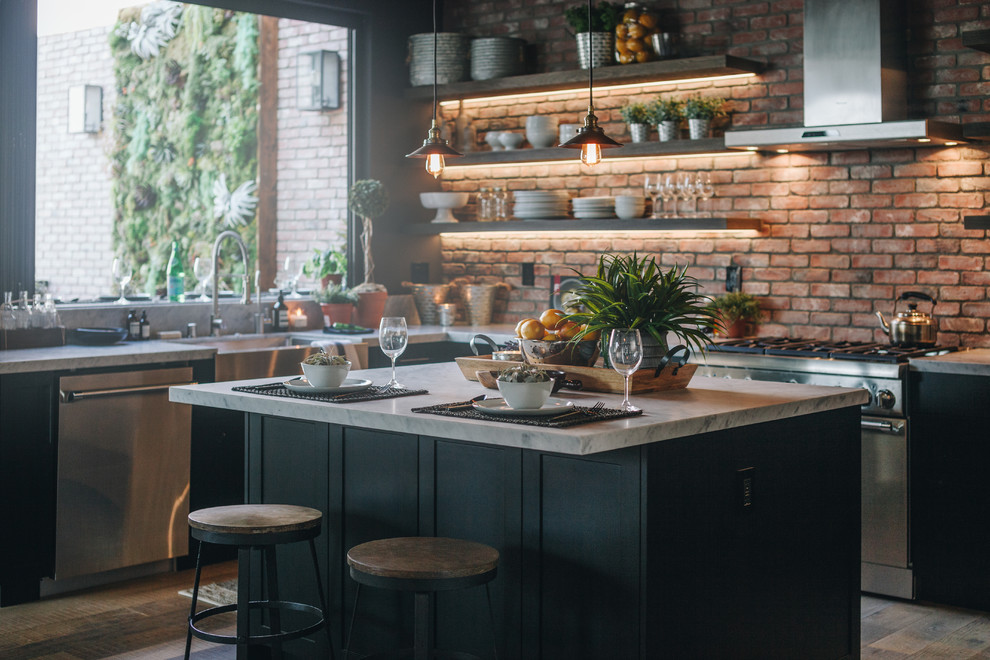Large urban l-shaped laminate floor and brown floor eat-in kitchen photo in Los Angeles with a farmhouse sink, shaker cabinets, black cabinets, red backsplash, brick backsplash, stainless steel appliances, an island and white countertops