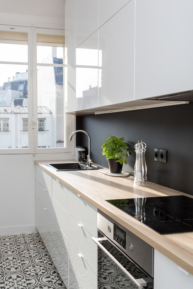 Inspiration for a mid-sized contemporary single-wall separate kitchen in Paris with wood benchtops, no island, a drop-in sink, flat-panel cabinets, white cabinets, black splashback, slate splashback, stainless steel appliances, slate floors, multi-coloured floor and beige benchtop.