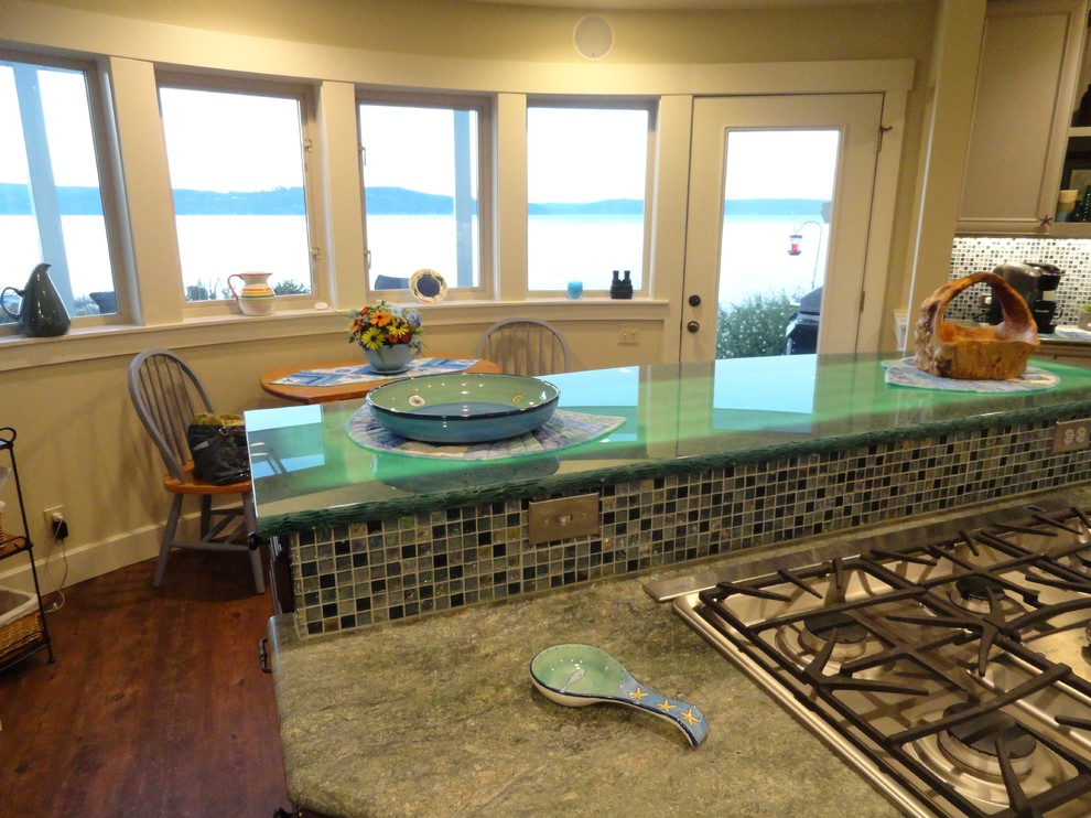 Photo of a large beach style u-shaped eat-in kitchen in Seattle with recycled glass benchtops, green splashback, glass sheet splashback, stainless steel appliances, raised-panel cabinets, dark wood cabinets, dark hardwood floors and with island.