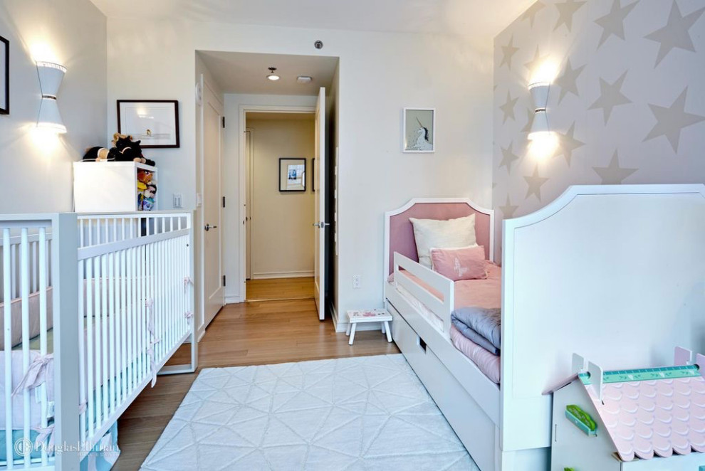 Example of a mid-sized trendy girl light wood floor, beige floor and wallpaper nursery design in Boston with white walls