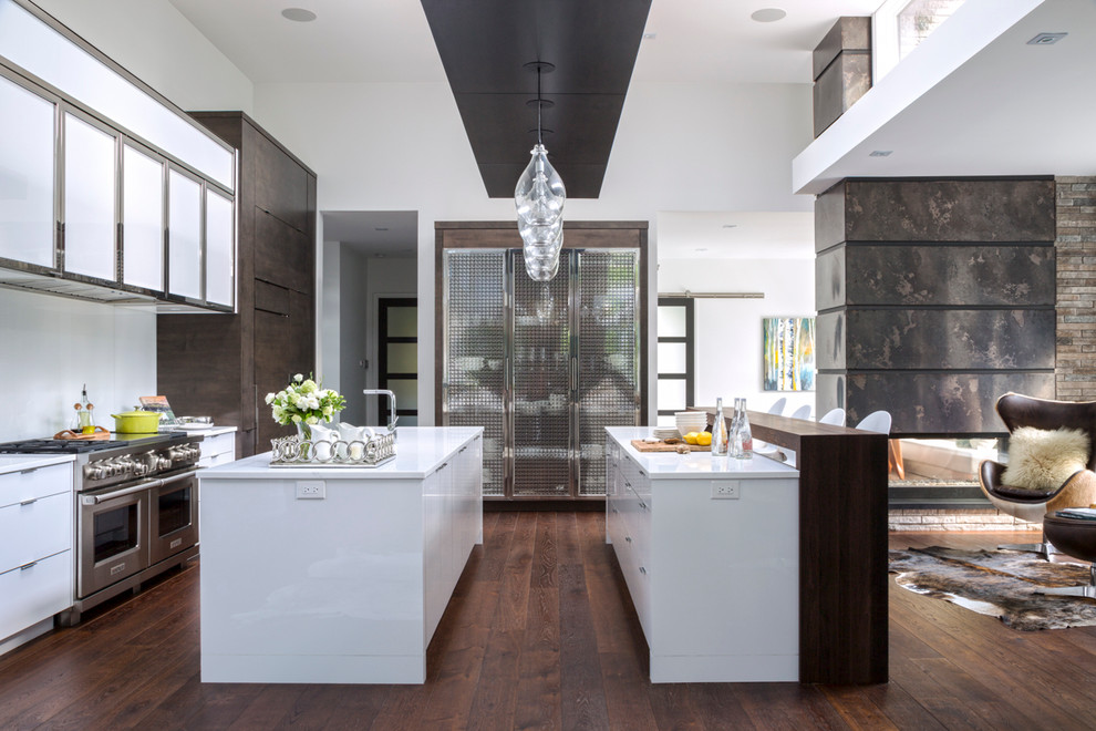 Photo of a contemporary galley open plan kitchen in Toronto with white cabinets, white splashback, stainless steel appliances, dark hardwood floors, multiple islands and flat-panel cabinets.