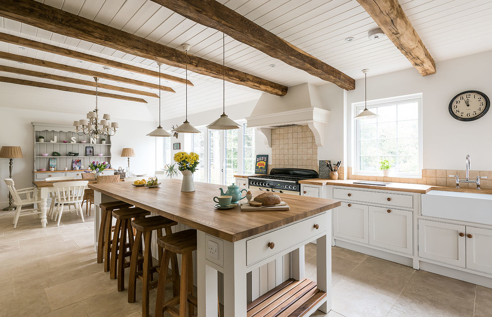 Inspiration for a country eat-in kitchen in London with a farmhouse sink, beaded inset cabinets, white cabinets, wood benchtops, beige splashback, ceramic splashback, with island and white appliances.