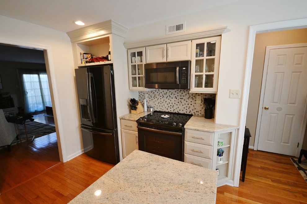This is an example of a mid-sized transitional l-shaped eat-in kitchen in Philadelphia with an undermount sink, recessed-panel cabinets, white cabinets, granite benchtops, multi-coloured splashback, mosaic tile splashback, black appliances, medium hardwood floors, a peninsula and brown floor.