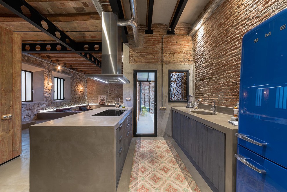 Inspiration for an industrial open plan kitchen in Barcelona with an integrated sink, flat-panel cabinets, concrete benchtops, red splashback, brick splashback, coloured appliances, concrete floors, a peninsula, grey floor and dark wood cabinets.