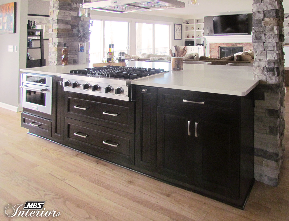 Example of a large transitional l-shaped light wood floor eat-in kitchen design with an undermount sink, recessed-panel cabinets, dark wood cabinets, quartz countertops, stainless steel appliances and an island