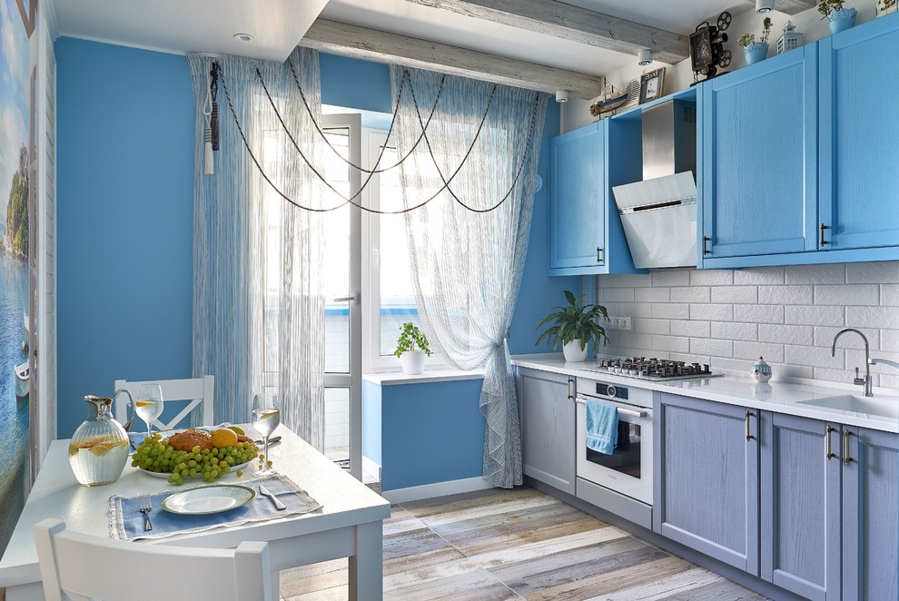Photo of a beach style eat-in kitchen in Other with an integrated sink, shaker cabinets, blue cabinets, grey splashback, subway tile splashback, white appliances, multi-coloured floor and white benchtop.