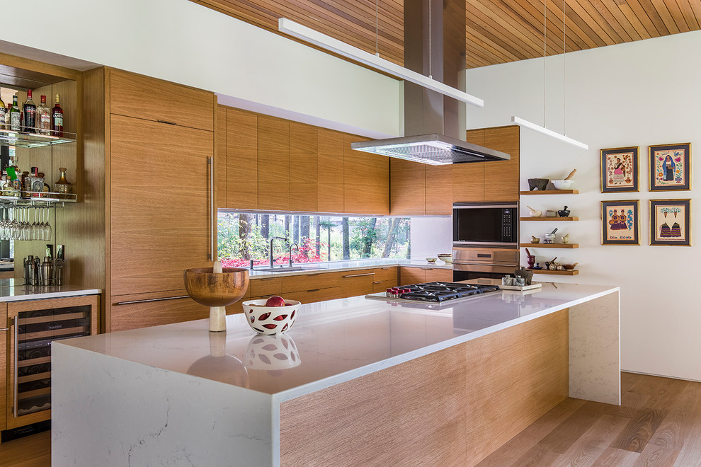 Photo of a contemporary l-shaped kitchen in Portland with an undermount sink, flat-panel cabinets, medium wood cabinets, window splashback, panelled appliances, medium hardwood floors, with island, brown floor and white benchtop.