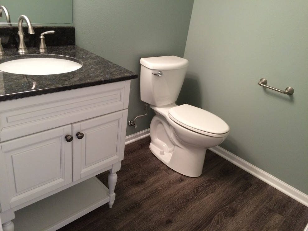 Mid-sized traditional powder room in Other with raised-panel cabinets, white cabinets, a two-piece toilet, green walls, dark hardwood floors, an undermount sink, granite benchtops and black benchtops.