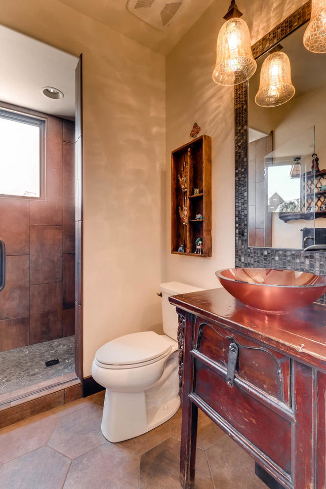 This is an example of a mid-sized 3/4 bathroom in Denver with furniture-like cabinets, distressed cabinets, an alcove shower, a two-piece toilet, multi-coloured tile, glass sheet wall, beige walls, ceramic floors and a vessel sink.