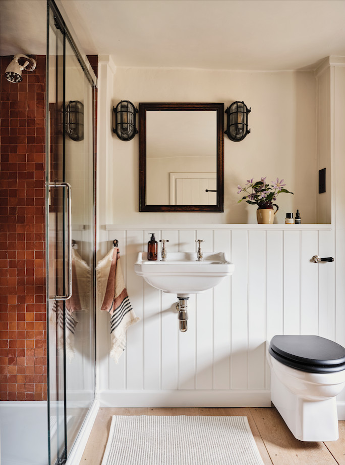 This is an example of a mid-sized country 3/4 bathroom in Oxfordshire with a curbless shower, a wall-mount toilet, brown tile, white walls, medium hardwood floors, a wall-mount sink, brown floor, a sliding shower screen, a single vanity and planked wall panelling.