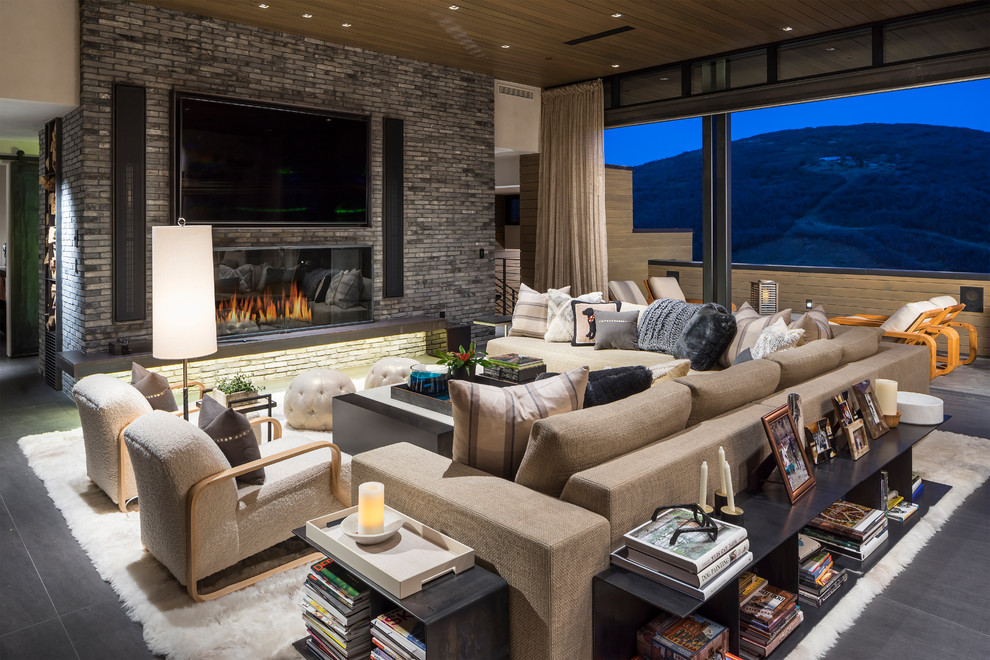 Photo of an expansive country living room in Salt Lake City with grey walls, a standard fireplace, a brick fireplace surround, a wall-mounted tv and grey floor.
