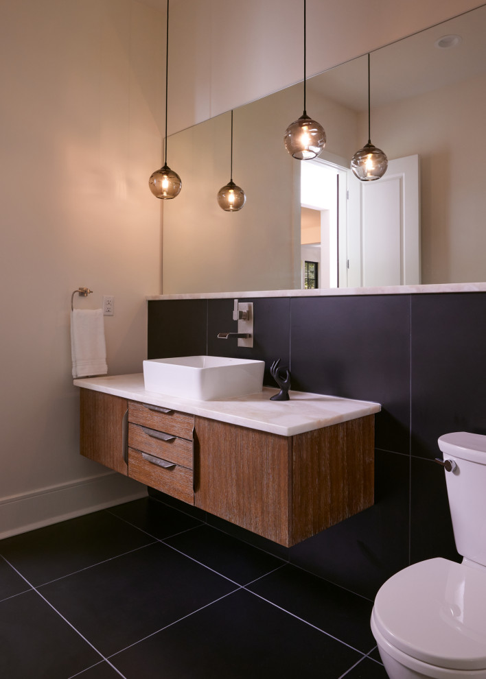 Cette image montre un grand WC et toilettes minimaliste en bois brun avec un placard en trompe-l'oeil, WC séparés, un carrelage noir, des carreaux de céramique, un mur beige, un sol en carrelage de céramique, une vasque, un plan de toilette en marbre, un sol noir, un plan de toilette blanc et meuble-lavabo suspendu.