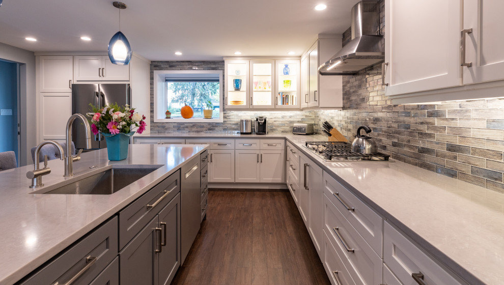 Design ideas for a mid-sized transitional l-shaped open plan kitchen in Philadelphia with an undermount sink, shaker cabinets, white cabinets, quartz benchtops, multi-coloured splashback, stainless steel appliances, medium hardwood floors, with island and grey benchtop.