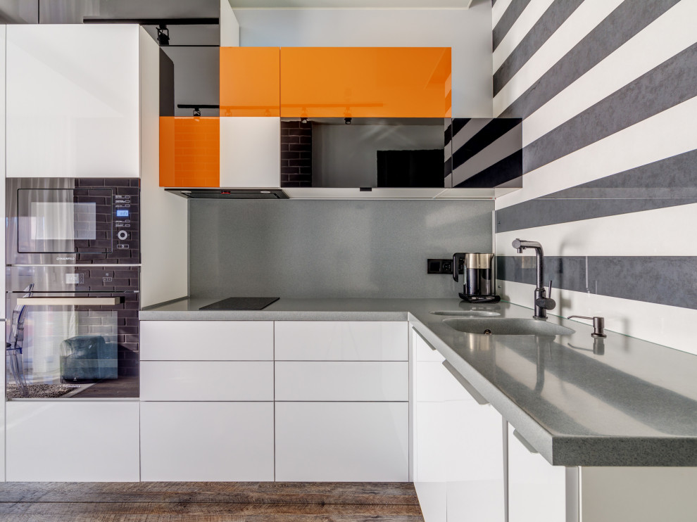 This is an example of a mid-sized contemporary l-shaped kitchen in Moscow with an integrated sink, flat-panel cabinets, white cabinets, grey splashback, black appliances, brown floor and grey benchtop.