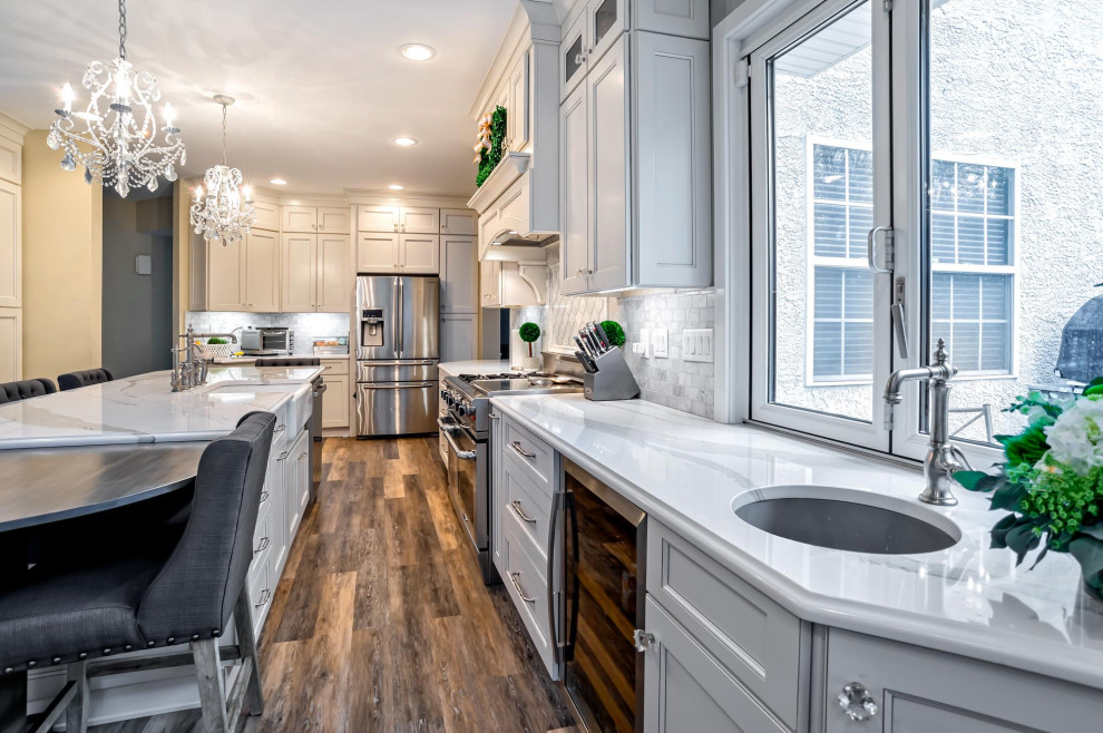 Example of a large transitional single-wall medium tone wood floor and brown floor eat-in kitchen design in Philadelphia with a farmhouse sink, shaker cabinets, white cabinets, quartz countertops, gray backsplash, porcelain backsplash, stainless steel appliances, an island and white countertops