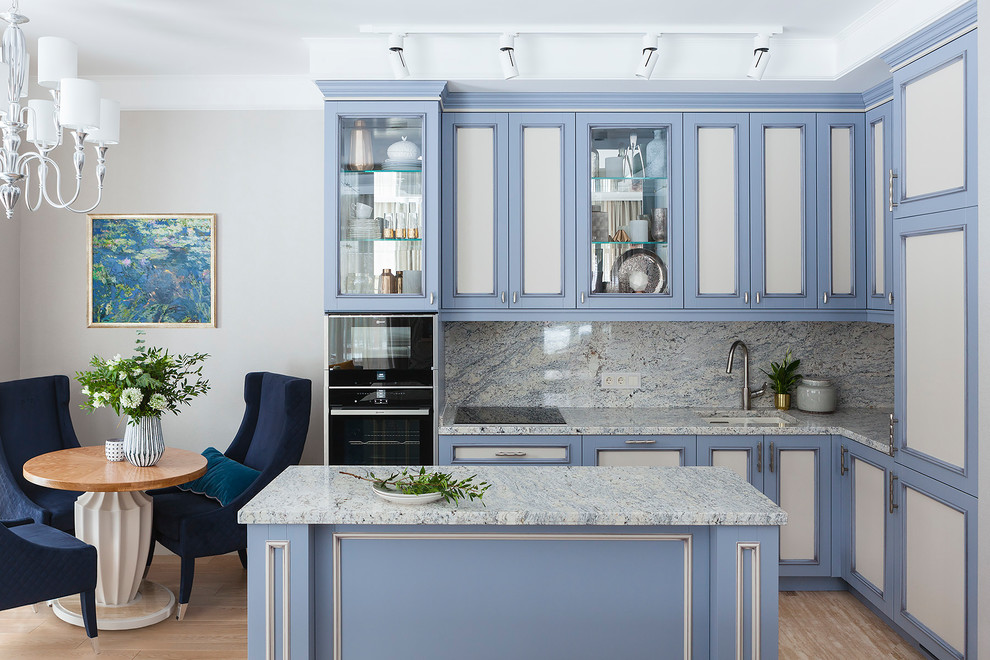 This is an example of a transitional l-shaped open plan kitchen in Moscow with an undermount sink, recessed-panel cabinets, blue cabinets, grey splashback, black appliances, with island, beige floor and grey benchtop.