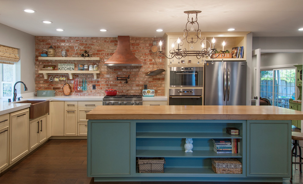 Mid-sized eclectic l-shaped open plan kitchen in San Francisco with a farmhouse sink, quartz benchtops, red splashback, stainless steel appliances, medium hardwood floors, with island, recessed-panel cabinets and beige cabinets.