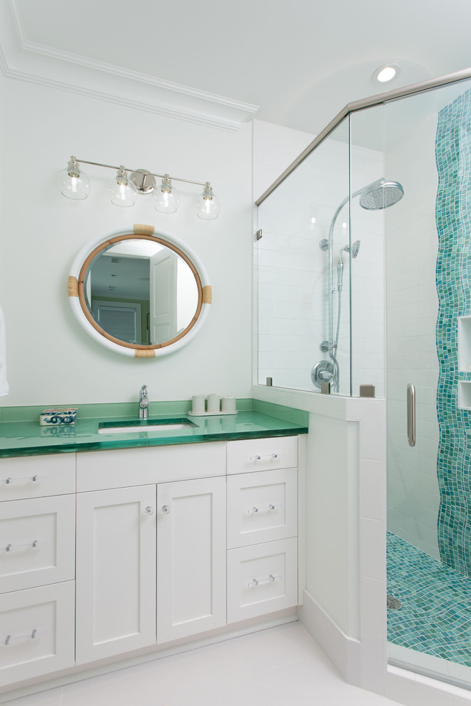 This is an example of a beach style 3/4 bathroom in Other with shaker cabinets, white cabinets, a corner shower, blue tile, mosaic tile, white walls, an undermount sink, glass benchtops, white floor, a hinged shower door and green benchtops.