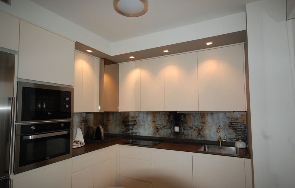 This is an example of a mid-sized transitional l-shaped separate kitchen in Other with a single-bowl sink, flat-panel cabinets, white cabinets, stainless steel appliances and no island.