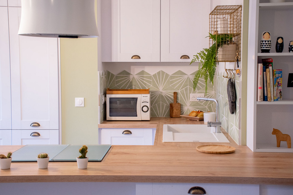 Foto på ett mellanstort funkis brun kök, med en enkel diskho, luckor med profilerade fronter, vita skåp, laminatbänkskiva, grönt stänkskydd, stänkskydd i cementkakel, rostfria vitvaror, ljust trägolv, en köksö och brunt golv