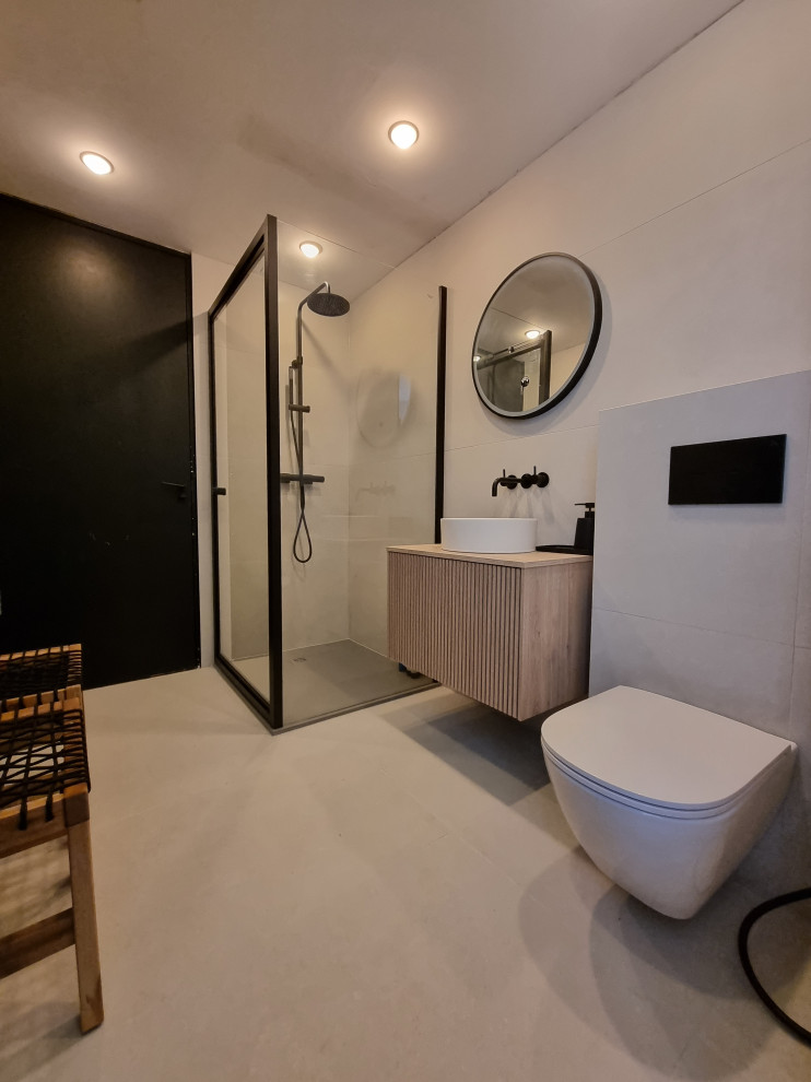 Photo of a small scandinavian master bathroom in Other with beaded inset cabinets, light wood cabinets, a corner shower, a wall-mount toilet, white tile, porcelain tile, white walls, pebble tile floors, a vessel sink, white floor, a hinged shower door, a single vanity and a floating vanity.