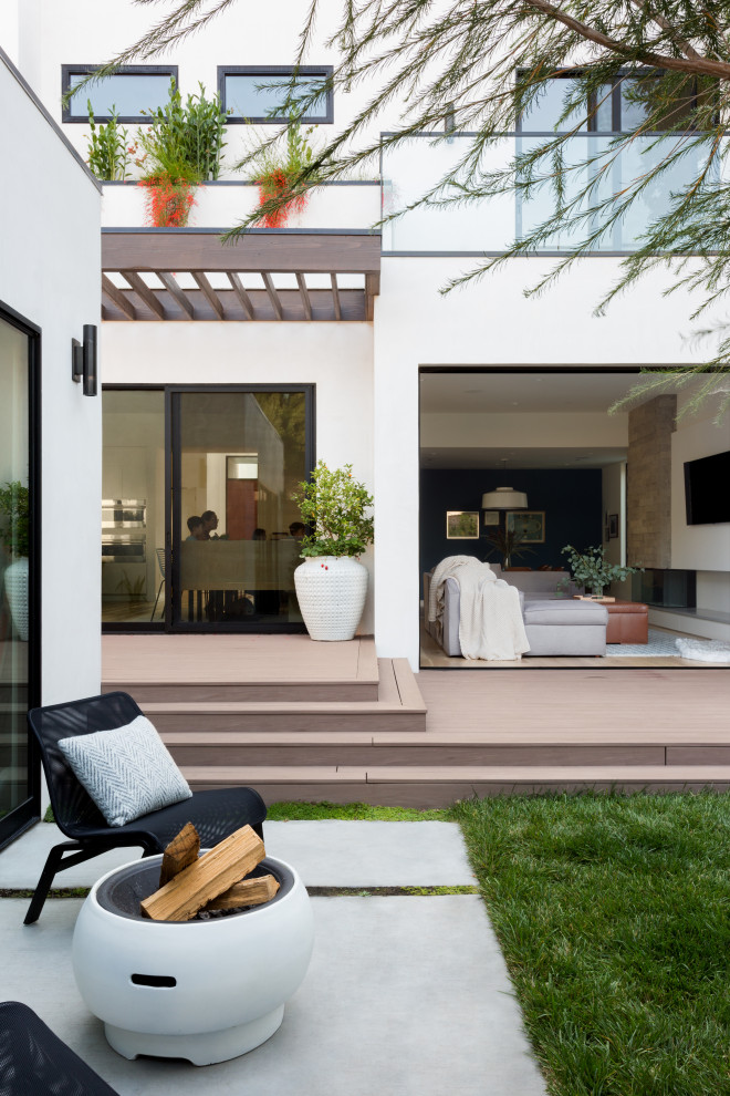 Cette photo montre une terrasse arrière et au rez-de-chaussée tendance de taille moyenne avec un foyer extérieur, une pergola et un garde-corps en verre.