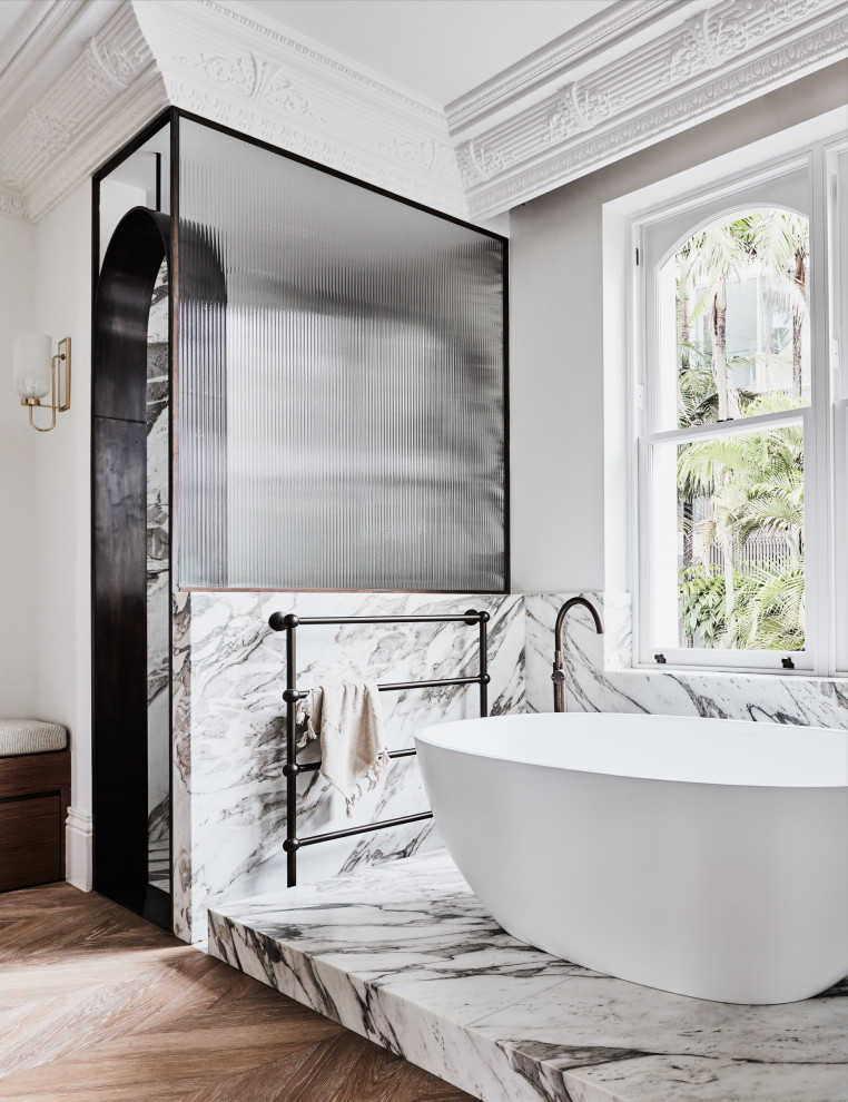 Exempel på ett klassiskt vit vitt en-suite badrum, med vita skåp, ett fristående badkar, en dusch i en alkov, en toalettstol med separat cisternkåpa, vit kakel, marmorkakel, vita väggar, mellanmörkt trägolv, ett avlångt handfat, marmorbänkskiva, brunt golv och dusch med gångjärnsdörr