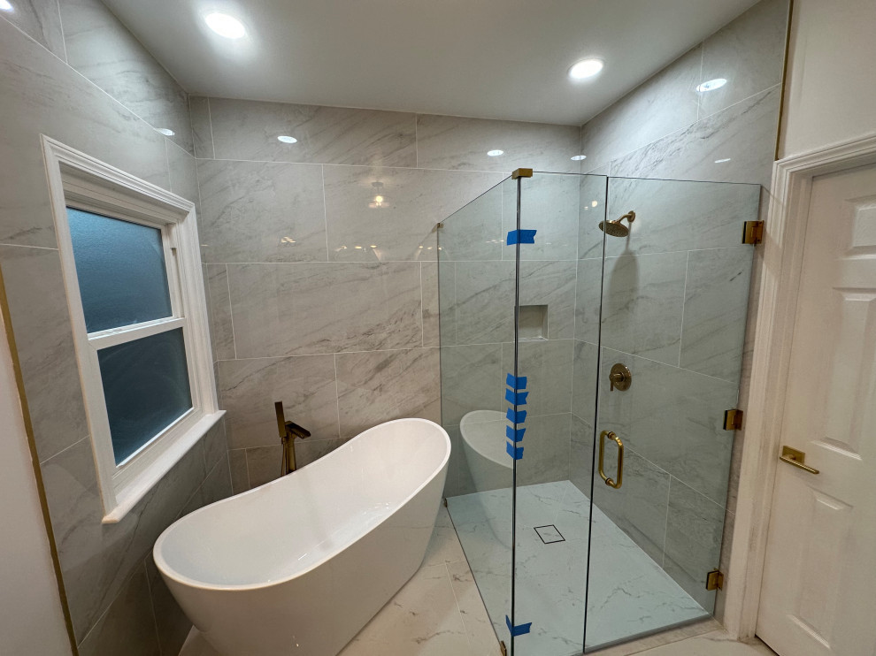 Marble-tiled bathroom with freestanding tub, glass shower enclosure, gold fixtures, and recessed lighting.