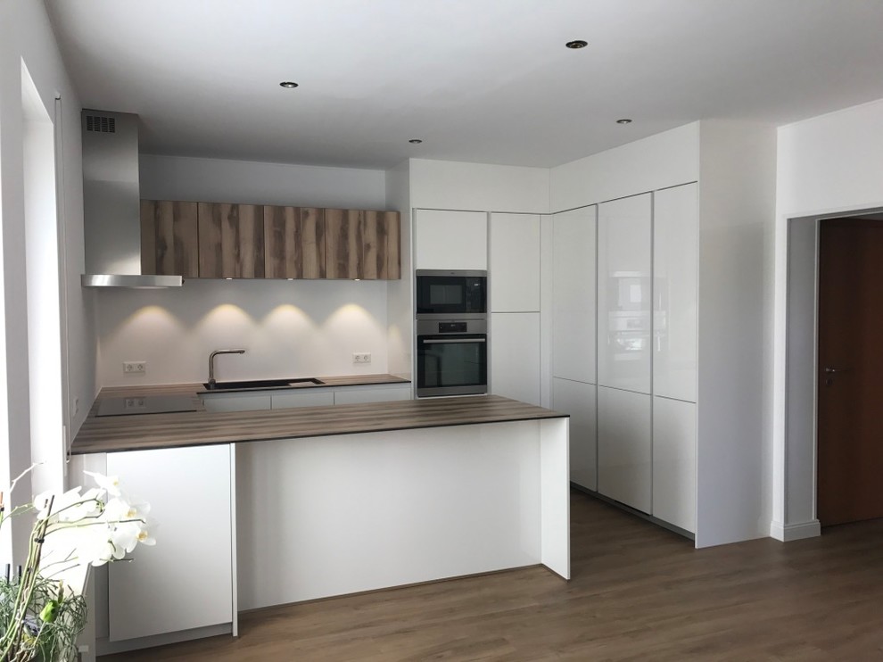 Design ideas for a mid-sized contemporary u-shaped open plan kitchen in Paris with an undermount sink, beaded inset cabinets, white cabinets, with island, white splashback, stainless steel appliances and medium hardwood floors.