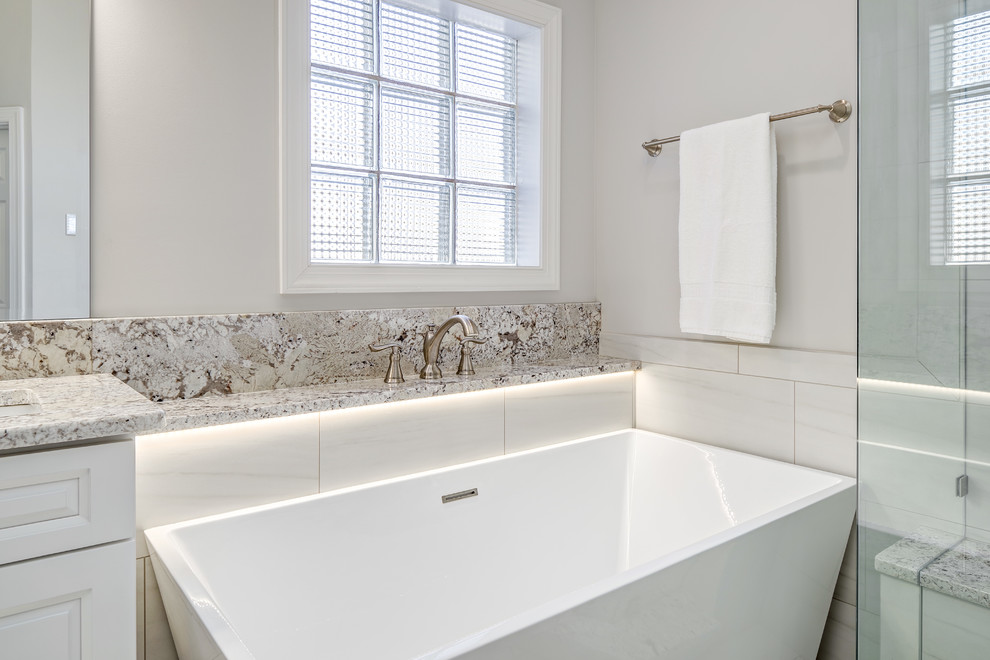 Large transitional master gray tile and porcelain tile porcelain tile and gray floor freestanding bathtub photo with raised-panel cabinets, white cabinets, a two-piece toilet, gray walls, an undermount sink, granite countertops and a hinged shower door