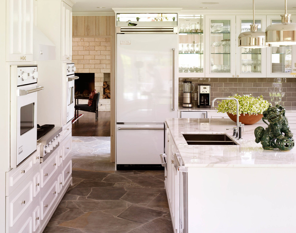 Inspiration for a traditional kitchen in Dallas with a double-bowl sink, glass-front cabinets, white cabinets, grey splashback, subway tile splashback, white appliances and slate floors.