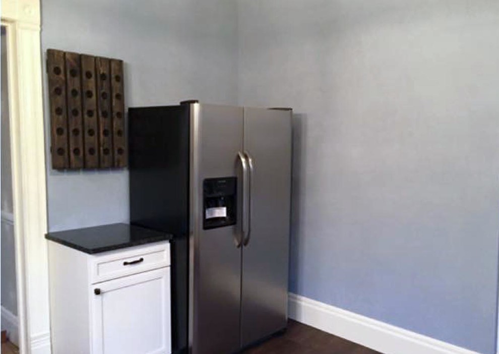 Inspiration for a mid-sized transitional l-shaped medium tone wood floor and brown floor kitchen pantry remodel with a farmhouse sink, recessed-panel cabinets, white cabinets, granite countertops, multicolored backsplash, glass tile backsplash, stainless steel appliances, no island and black countertops
