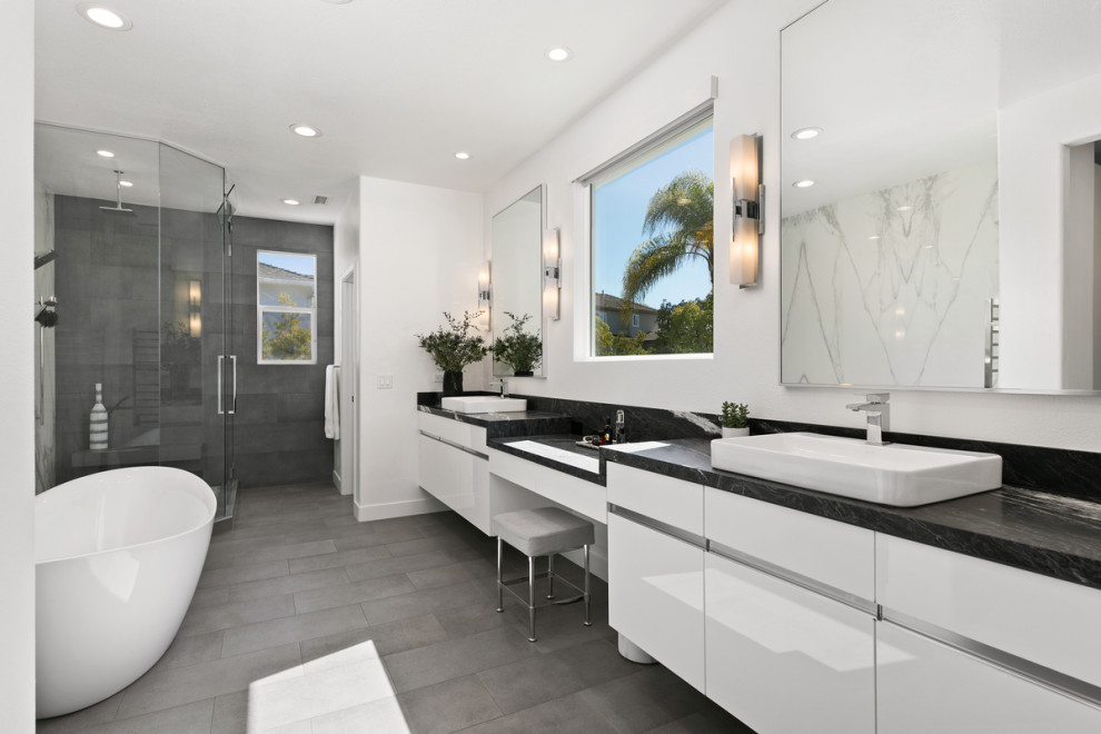 Large beach style master white tile and porcelain tile porcelain tile, gray floor and double-sink bathroom photo in San Diego with flat-panel cabinets, white cabinets, a one-piece toilet, white walls, a vessel sink, marble countertops, a hinged shower door, black countertops and a floating vanity