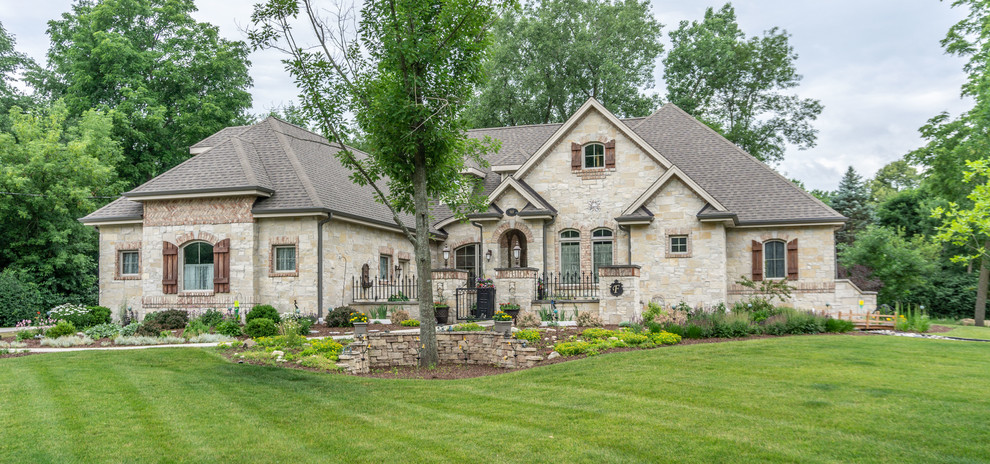 Photo of a large transitional two-storey beige house exterior in Milwaukee with stone veneer, a hip roof and a shingle roof.