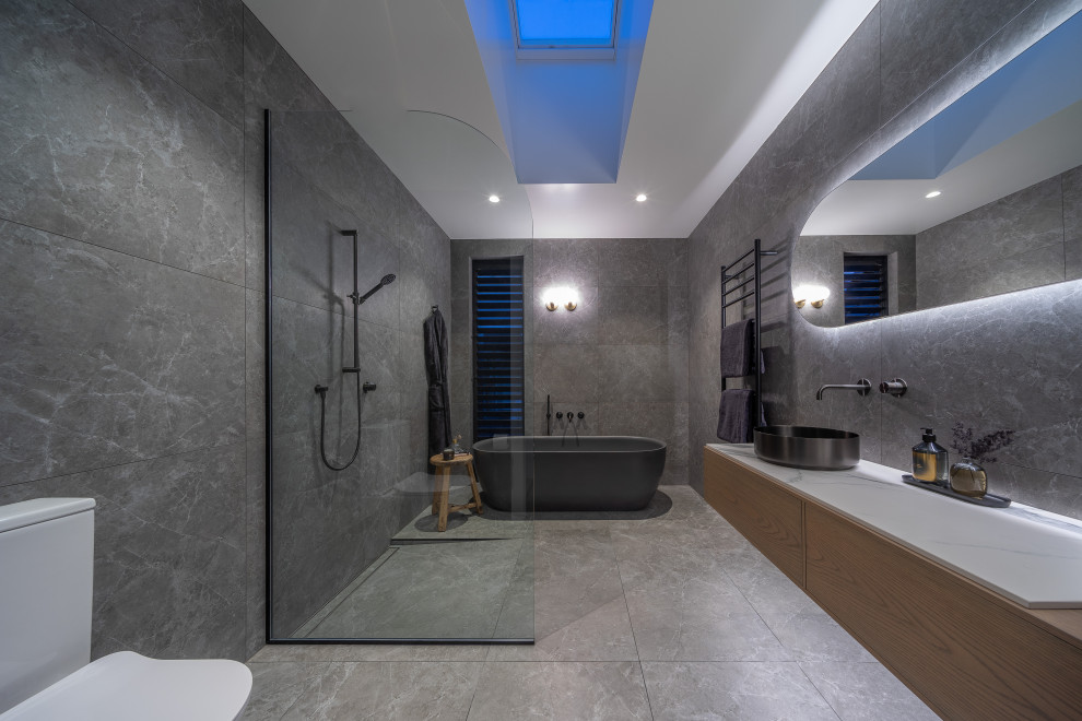 Стильный дизайн: большая ванная комната в современном стиле с плоскими фасадами, черными фасадами, отдельно стоящей ванной, открытым душем, унитазом-моноблоком, черно-белой плиткой, каменной плиткой, черными стенами, полом из керамической плитки, душевой кабиной, настольной раковиной, черным полом, открытым душем, белой столешницей, тумбой под одну раковину, подвесной тумбой, кессонным потолком и панелями на части стены - последний тренд