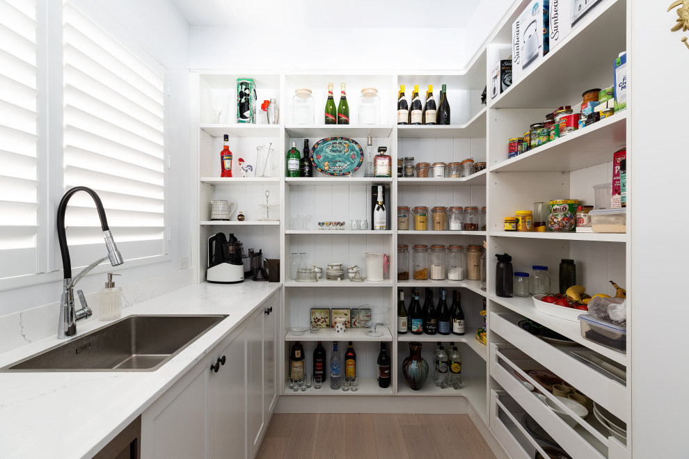 This is an example of a medium sized beach style single-wall kitchen pantry in Sydney with a built-in sink, recessed-panel cabinets, white cabinets, granite worktops, white splashback, granite splashback, stainless steel appliances, light hardwood flooring, beige floors and white worktops.