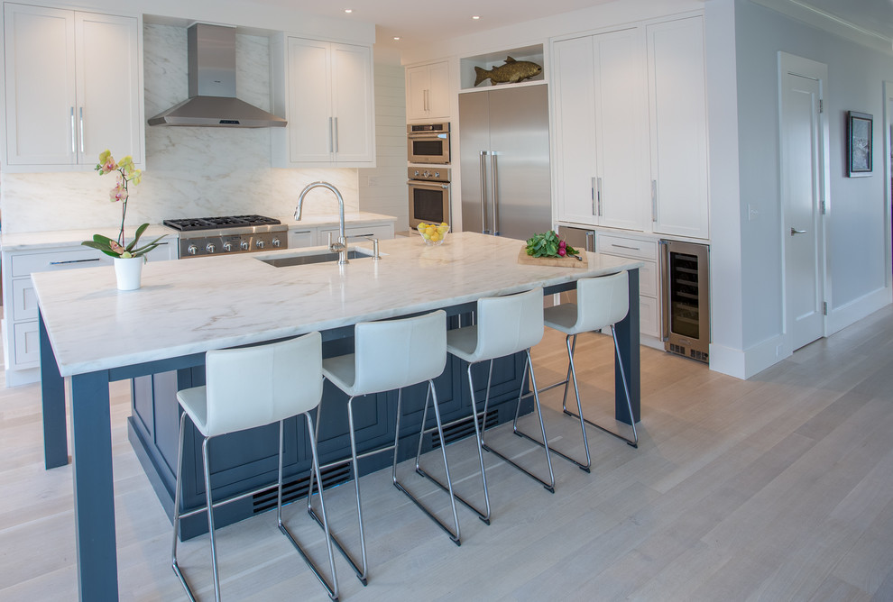 Photo of a mid-sized transitional galley eat-in kitchen in New York with beaded inset cabinets, white cabinets, marble benchtops, white splashback, stone tile splashback, stainless steel appliances, light hardwood floors and with island.