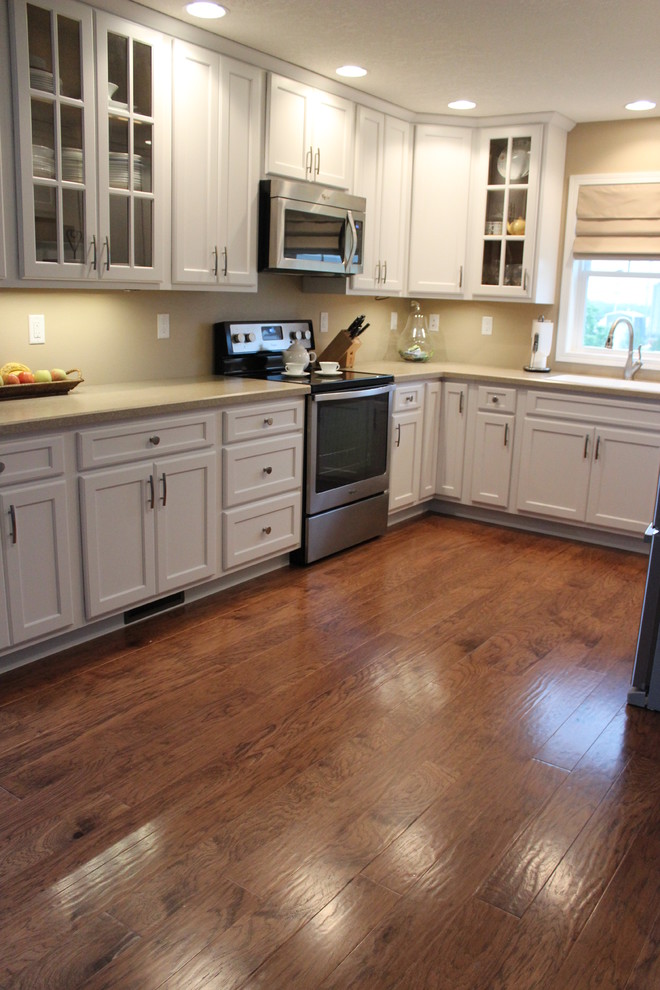 Inspiration for a mid-sized transitional l-shaped dark wood floor and brown floor eat-in kitchen remodel in Cedar Rapids with a double-bowl sink, shaker cabinets, white cabinets, quartz countertops, beige backsplash, stone slab backsplash, stainless steel appliances and an island
