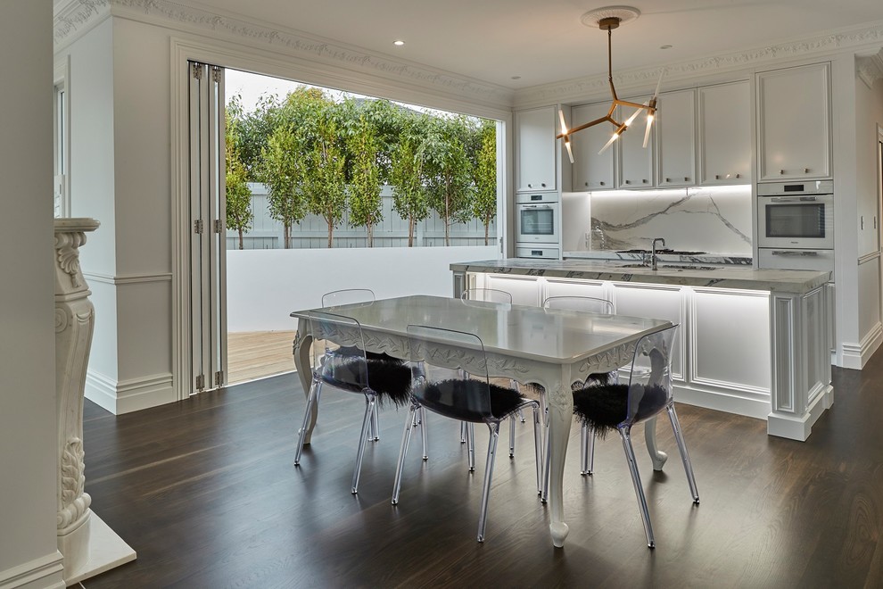 Contemporary galley eat-in kitchen in Auckland with an undermount sink, recessed-panel cabinets, white cabinets, white appliances, dark hardwood floors, with island, brown floor and white benchtop.