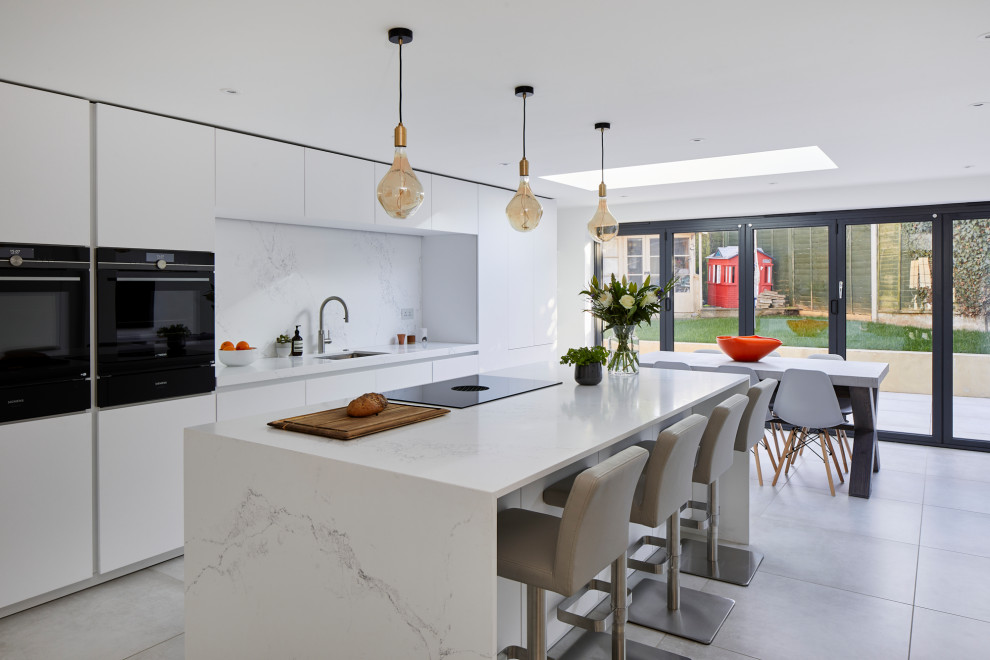 Inspiration for a large contemporary single-wall open plan kitchen in Kent with an undermount sink, flat-panel cabinets, white cabinets, quartz benchtops, white splashback, engineered quartz splashback, stainless steel appliances, ceramic floors, with island and white benchtop.