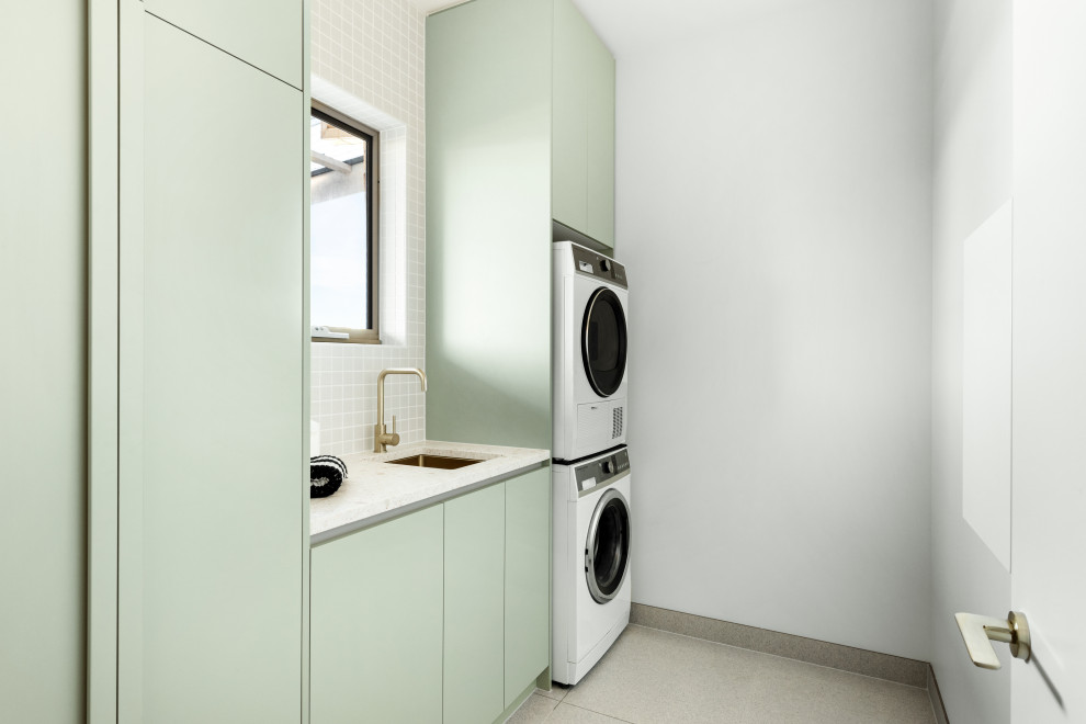 Mid-sized contemporary single-wall laundry room in Melbourne with green cabinets, terrazzo benchtops, green splashback, white walls, a stacked washer and dryer and white benchtop.