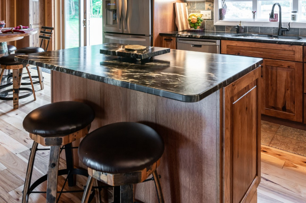 Mountain style l-shaped medium tone wood floor kitchen photo in Boston with an undermount sink, raised-panel cabinets, medium tone wood cabinets, granite countertops, gray backsplash, stainless steel appliances, an island and black countertops