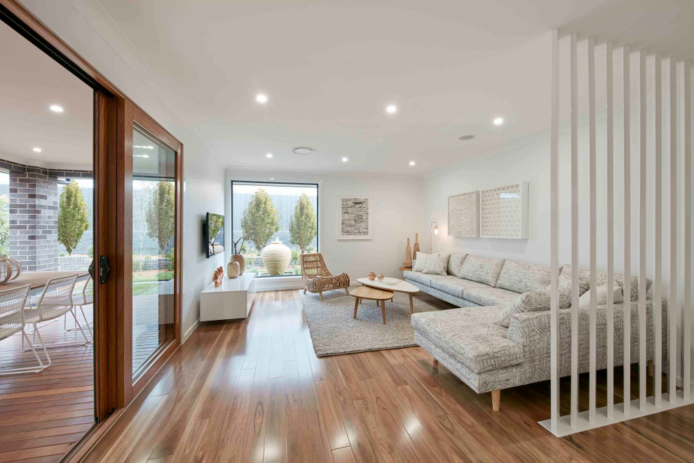 Photo of a contemporary open concept living room in Sydney with white walls, medium hardwood floors, no fireplace, a wall-mounted tv and brown floor.
