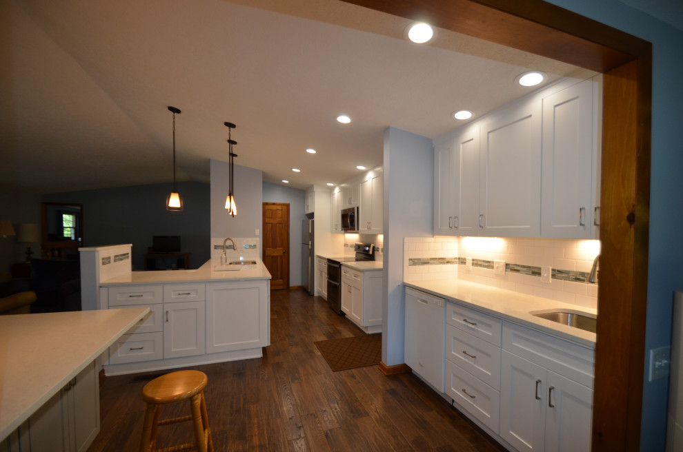 Example of a mid-sized transitional u-shaped medium tone wood floor and brown floor eat-in kitchen design with an undermount sink, raised-panel cabinets, beige cabinets, quartz countertops, white backsplash, subway tile backsplash, stainless steel appliances, an island and white countertops