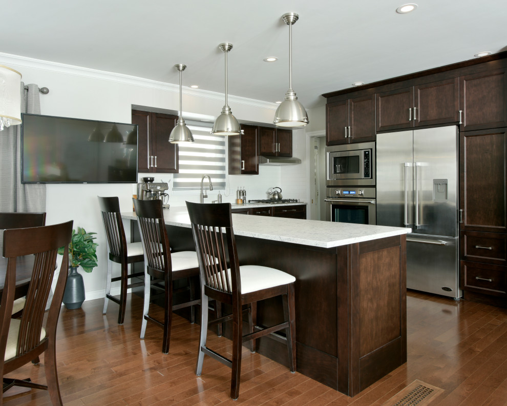 Photo of a mid-sized traditional l-shaped eat-in kitchen in Ottawa with shaker cabinets, dark wood cabinets, white splashback, stainless steel appliances, dark hardwood floors and with island.